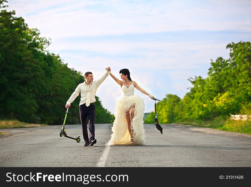 Smiling young newlywed couple with scooter on countryside road. Smiling young newlywed couple with scooter on countryside road