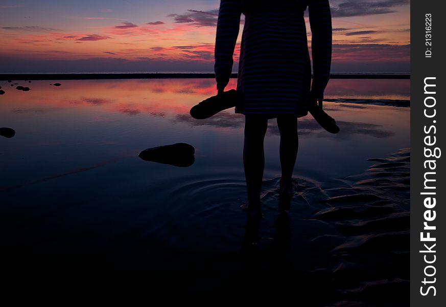 Silhouette of a child standing in a beach pool with beautiful sunset.