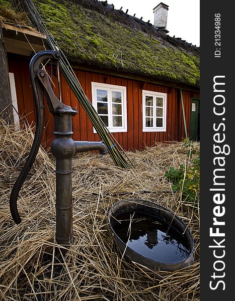 An old water pump on a farm with a red cottage in the background