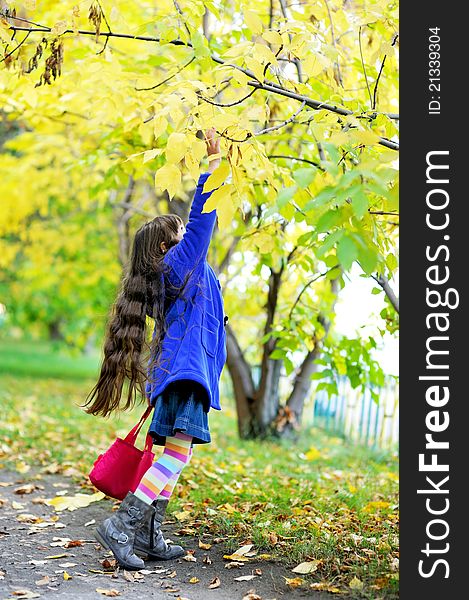 Funky little girl in blue coat standing on tiptoe under the yellow tree. Funky little girl in blue coat standing on tiptoe under the yellow tree
