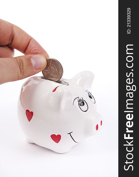 Hand inserting a coin in a piggy bank against a white background. Hand inserting a coin in a piggy bank against a white background