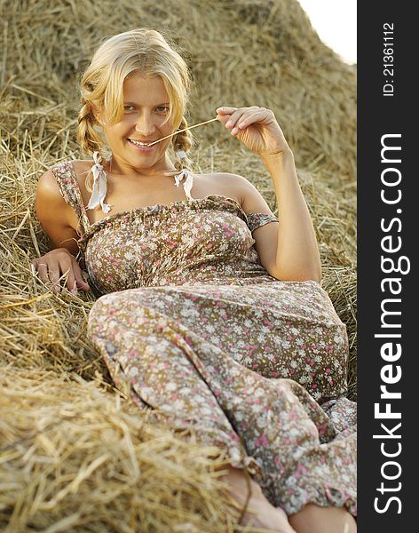 Portrait of beautiful blonde country girl sittitng on hay in light of sunset