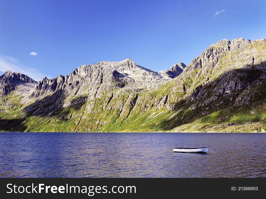 A lonely wooden fishing boat under the massive Scandinavian fjords - rugged mountains under blue skies. A lonely wooden fishing boat under the massive Scandinavian fjords - rugged mountains under blue skies