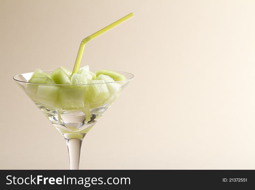 Pieces of honeydew green melon in a martini glass with straw on a beige background. Pieces of honeydew green melon in a martini glass with straw on a beige background