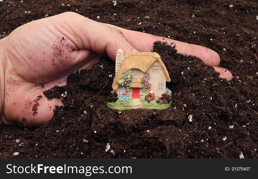 Hand of a man presenting a small country house on a pile of brown soil. Hand of a man presenting a small country house on a pile of brown soil