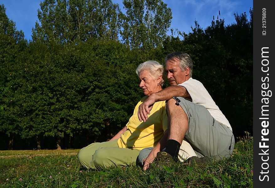 Senior couple sitting and relaxing on a glade on a beautiful sunny afternoon, with woods in the background. Senior couple sitting and relaxing on a glade on a beautiful sunny afternoon, with woods in the background.