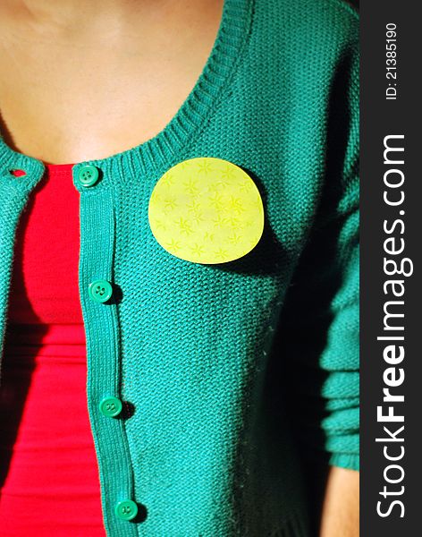 Close up of a blank yellow sticker on person wearing a green vest with a red t-shirt. Close up of a blank yellow sticker on person wearing a green vest with a red t-shirt