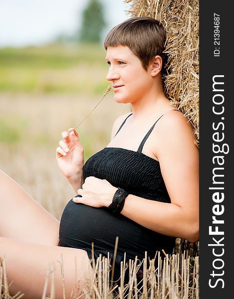 Pregnant woman with big belly and straw on the field. Pregnant woman with big belly and straw on the field