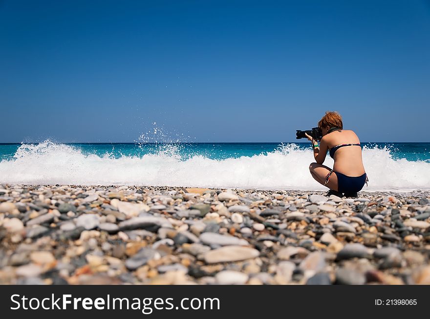 Girl with a camera takes pictures at the beach against the waves of the sea. Girl with a camera takes pictures at the beach against the waves of the sea