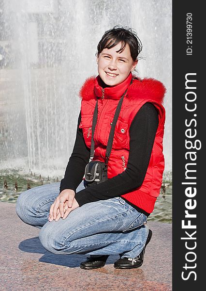 The girl in a red jacket sits against a city fountain. The girl in a red jacket sits against a city fountain