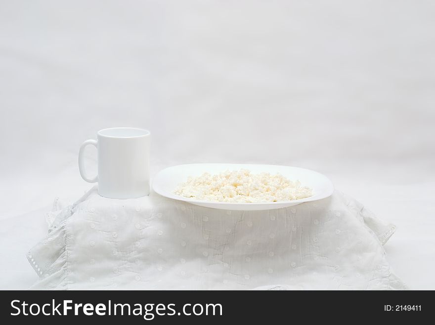 White table with curd on white plate and white cup on the white background. White table with curd on white plate and white cup on the white background