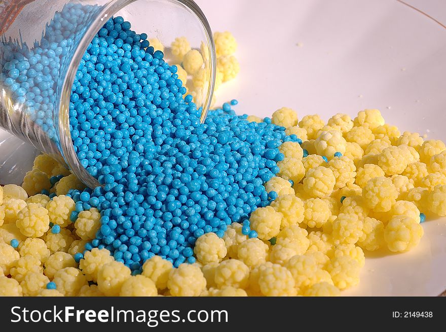 Small blue candies in a small glass on a saucer with yellow candies