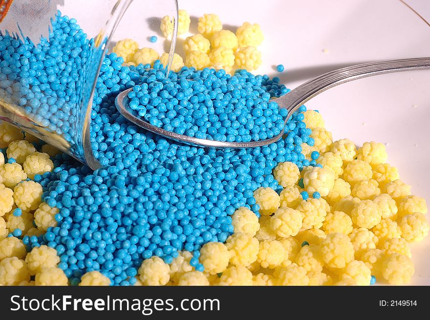 Small blue candies in a small glass on a saucer with yellow candies and teaspoon