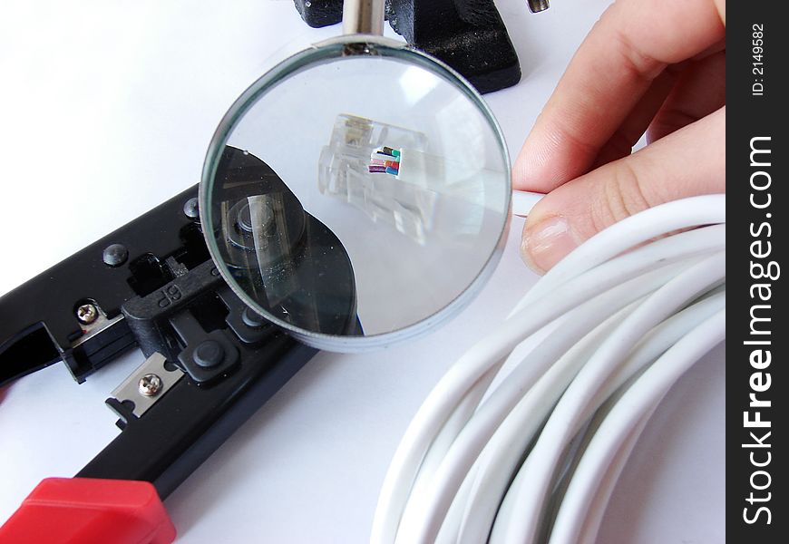 Hands cheking the network cable (cat5e) under a magnifier& crimper is under it. Hands cheking the network cable (cat5e) under a magnifier& crimper is under it.