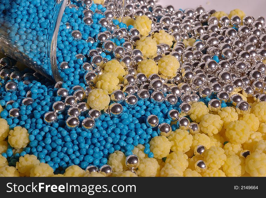 Small blue candies in a small glass on a saucer with yellow and silver candies