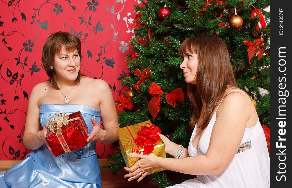 Two young  women with gifts near a new-year tree