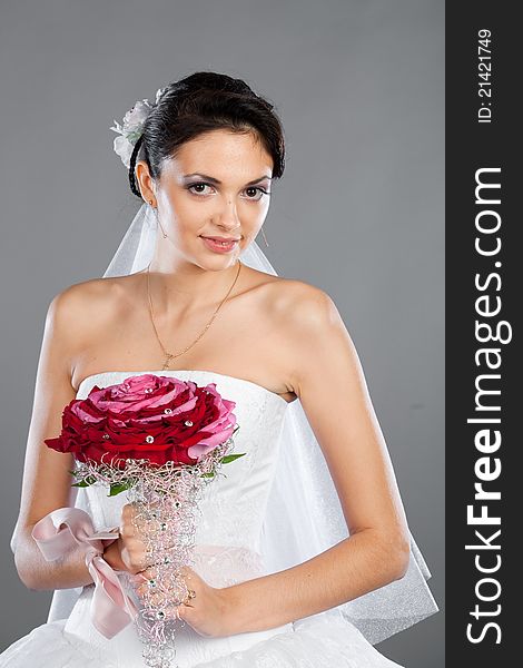 Beautiful brunette bride with a bouquet in the studio on a gray background