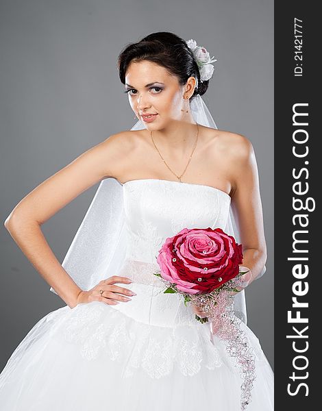 Beautiful brunette bride with a bouquet in the studio on a gray background