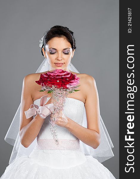 Beautiful brunette bride with a bouquet in the studio on a gray background