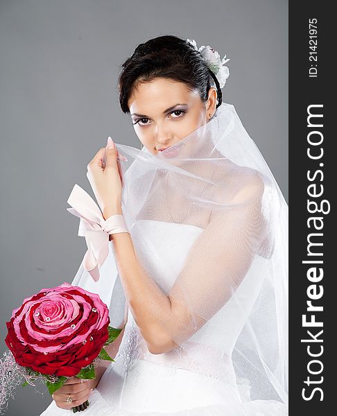 Beautiful brunette bride with a bouquet in the studio on a gray background
