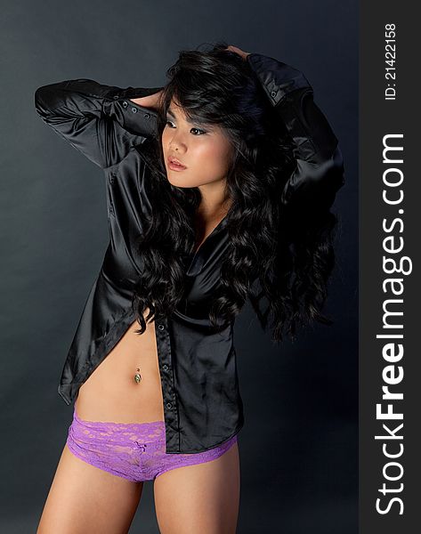 A fashion portrait of an attractive young woman wearing a shiny black top that exposes her stomach, and lacy purple panties. A fashion portrait of an attractive young woman wearing a shiny black top that exposes her stomach, and lacy purple panties