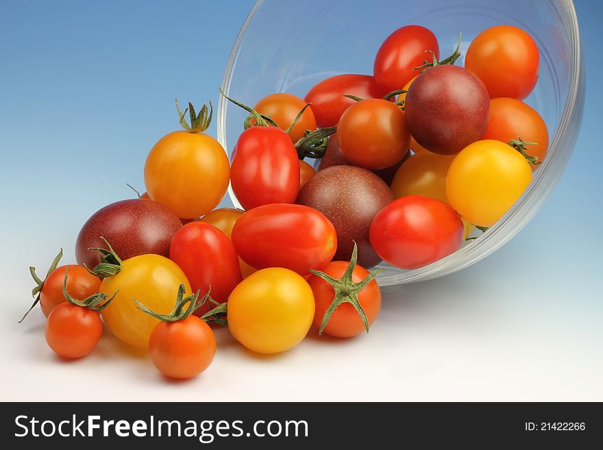 A variety of Cherry tomatoes spill out of a glass bowl.