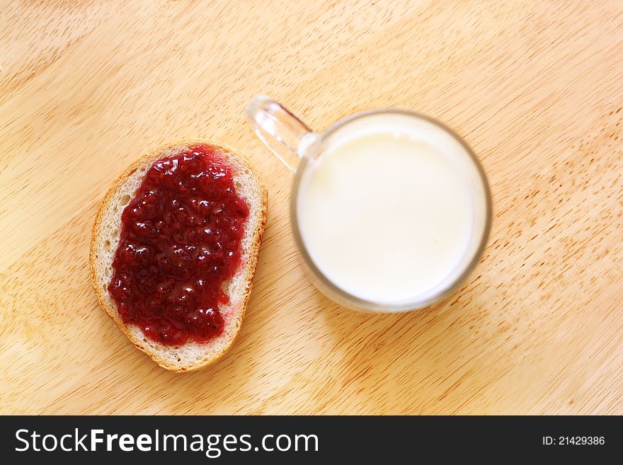 Bread with jam and glass of milk on wooden table