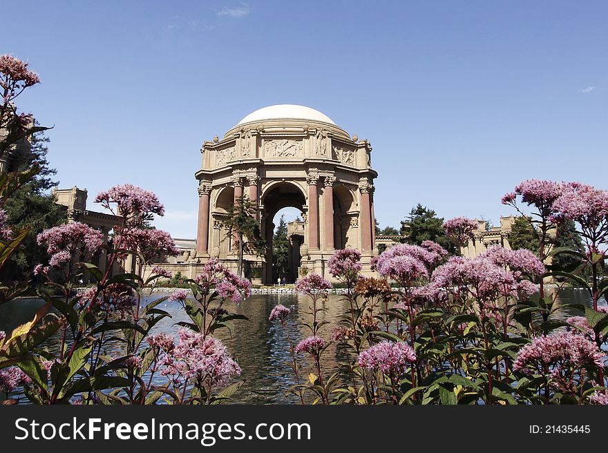 Palace of Fine Arts in San Francisco,California, view across pond, foreground framed by pink flowers.