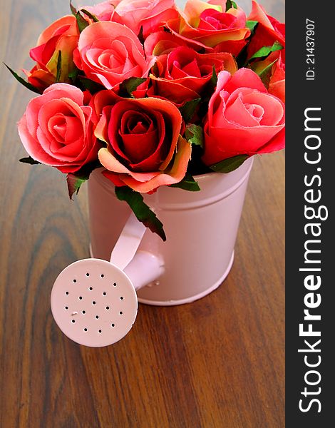 Plastic bouquet roses in watering can on wood background