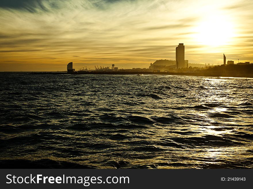 Bright yellow sundown seascape with silhouettes of Barcelona’s high-rise buildings and harbor cranes on the background. Bright yellow sundown seascape with silhouettes of Barcelona’s high-rise buildings and harbor cranes on the background