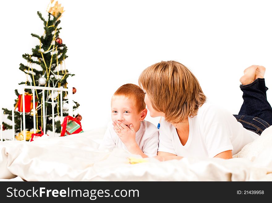 Mother with a son near a new-year tree on a white bed