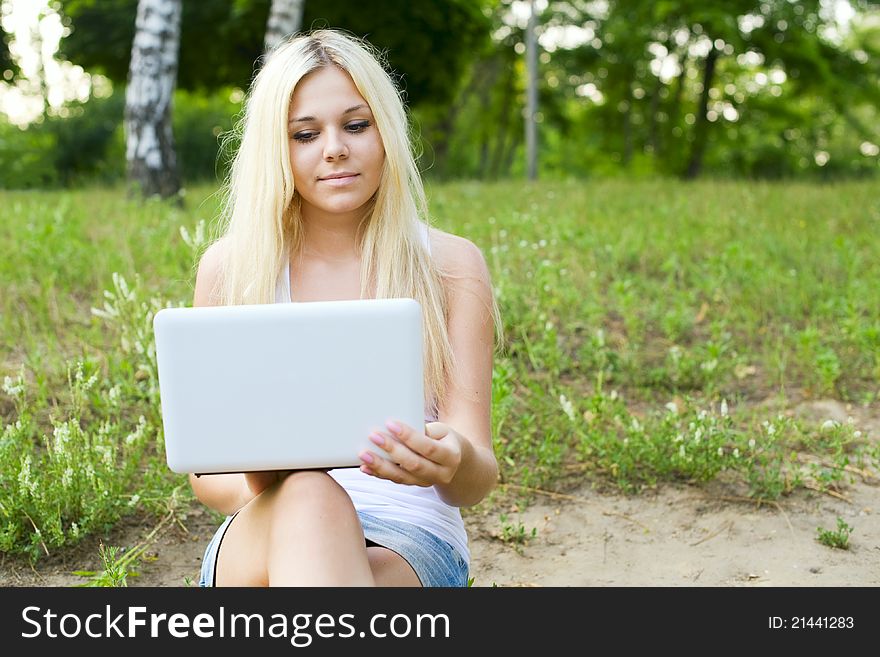 Portrait of a cheerful young woman sitting on lawn with a laptop. Portrait of a cheerful young woman sitting on lawn with a laptop