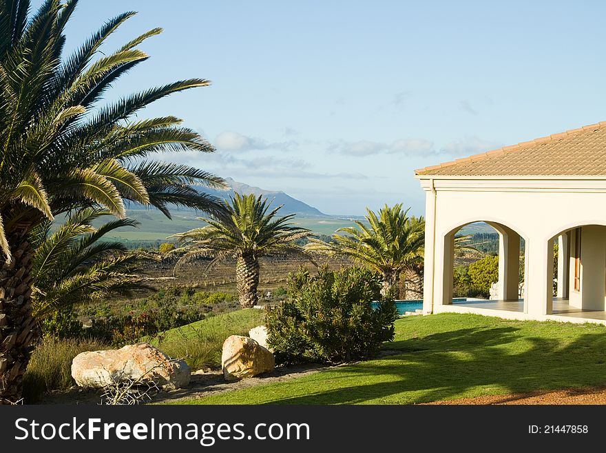 View past the verandah of a summer villa onto the blue sparkling swimming pool and mountain landscape in the distance. View past the verandah of a summer villa onto the blue sparkling swimming pool and mountain landscape in the distance