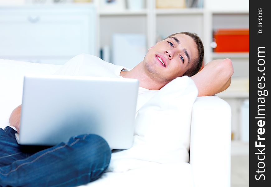 Handsome young man using laptop and lying on the sofa