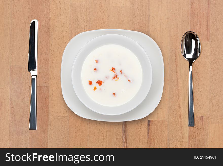 A plate of milk soup with vegetables on a wooden table with spoon and knife.