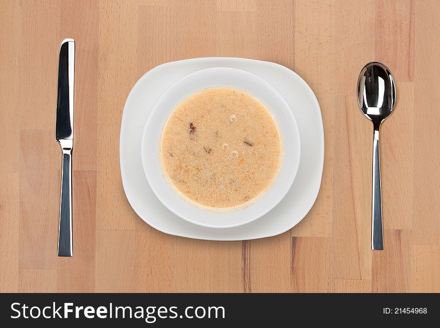 A plate of soup with a spoon and knife on a wooden table. A plate of soup with a spoon and knife on a wooden table.