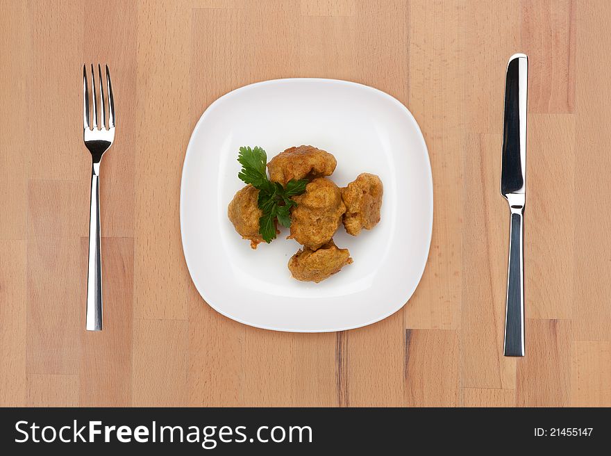 A plate of cooked battered cauliflower on a wooden table with fork and knife.