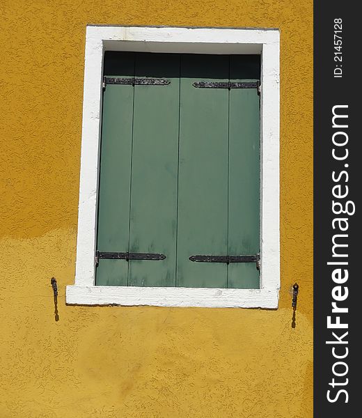 A green shuttered window, bordered by a white frame, in a yellow colored wall. A green shuttered window, bordered by a white frame, in a yellow colored wall.