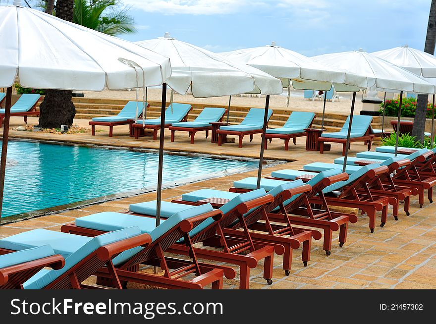 Many wooden lounge chairs in row around swimming pool