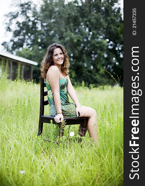 A smiling beautiful girl sitting on a chair in a field. A smiling beautiful girl sitting on a chair in a field.