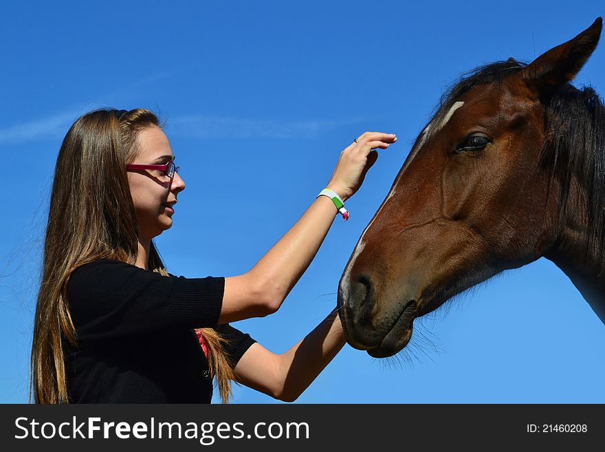 A long haired young woman caressing a brown horse with the sky in the background. A long haired young woman caressing a brown horse with the sky in the background.