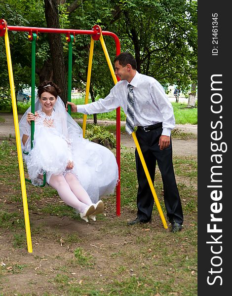 Bride sitting on swings and groom standing near