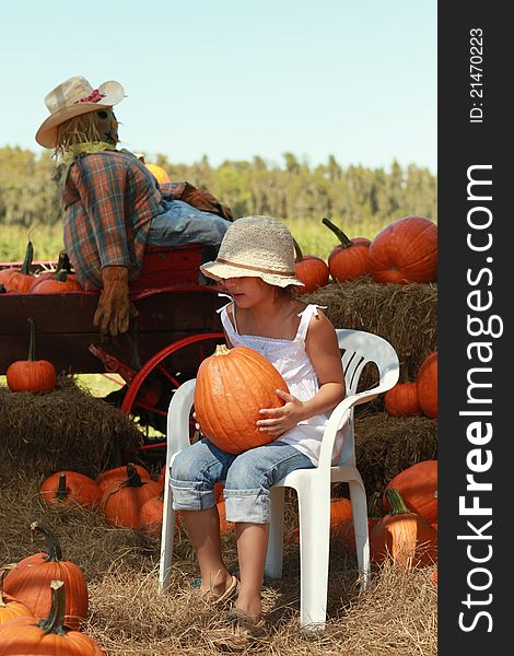 A young girl sitting in a chair holding a pumpkin at a Halloween pumpkin patch. A young girl sitting in a chair holding a pumpkin at a Halloween pumpkin patch.