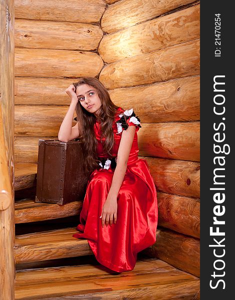 Girl in red spanish dress sitting on stairs with suitcase in old wooden house