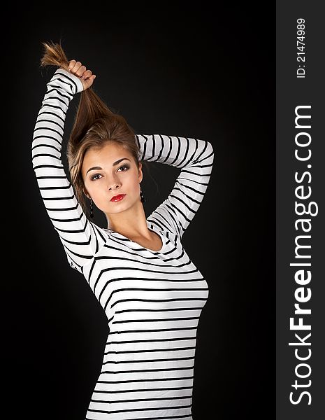 Beautiful girl in a striped dress pulls his hair on a black background