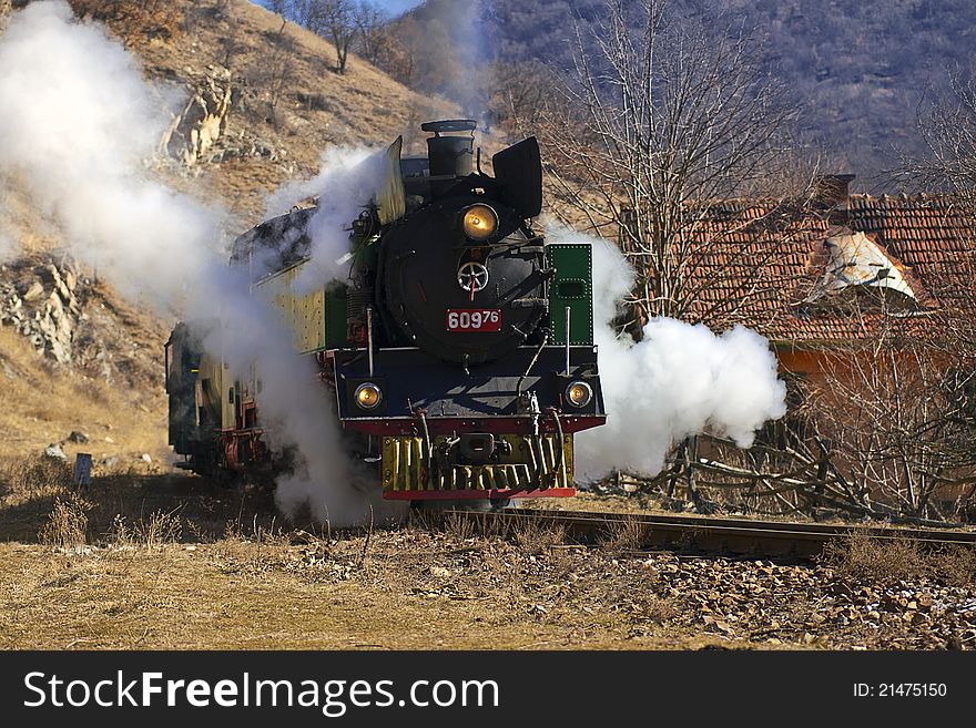 Steam train from late nineteenth century in sunny winter next to country home. Green and red retro locomotive.