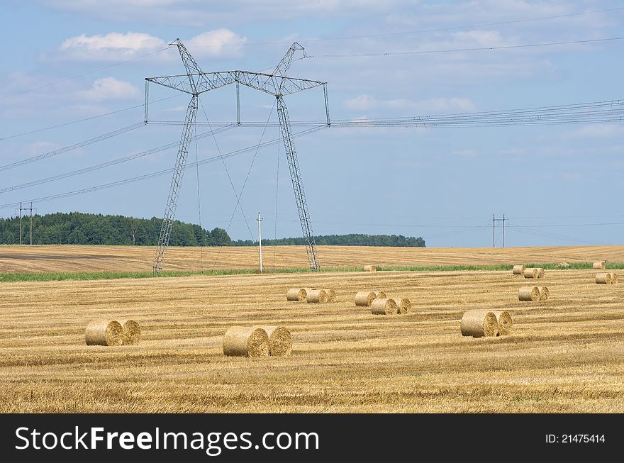The high-voltage line running through a field with rolls of straw. The high-voltage line running through a field with rolls of straw