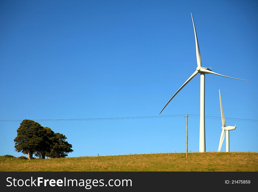 Two wind turbines in a paddock set against a blue sky