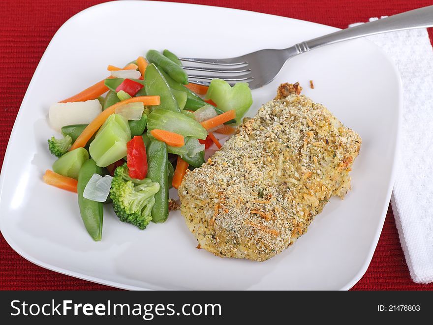 Breaded fish fillet and vegetables on a white plate