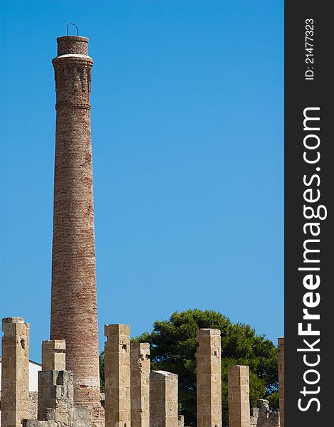 A single brick smoke stack, old and dirty, against an overcast blue sky and enclose some pillars, near natural oasis. A single brick smoke stack, old and dirty, against an overcast blue sky and enclose some pillars, near natural oasis